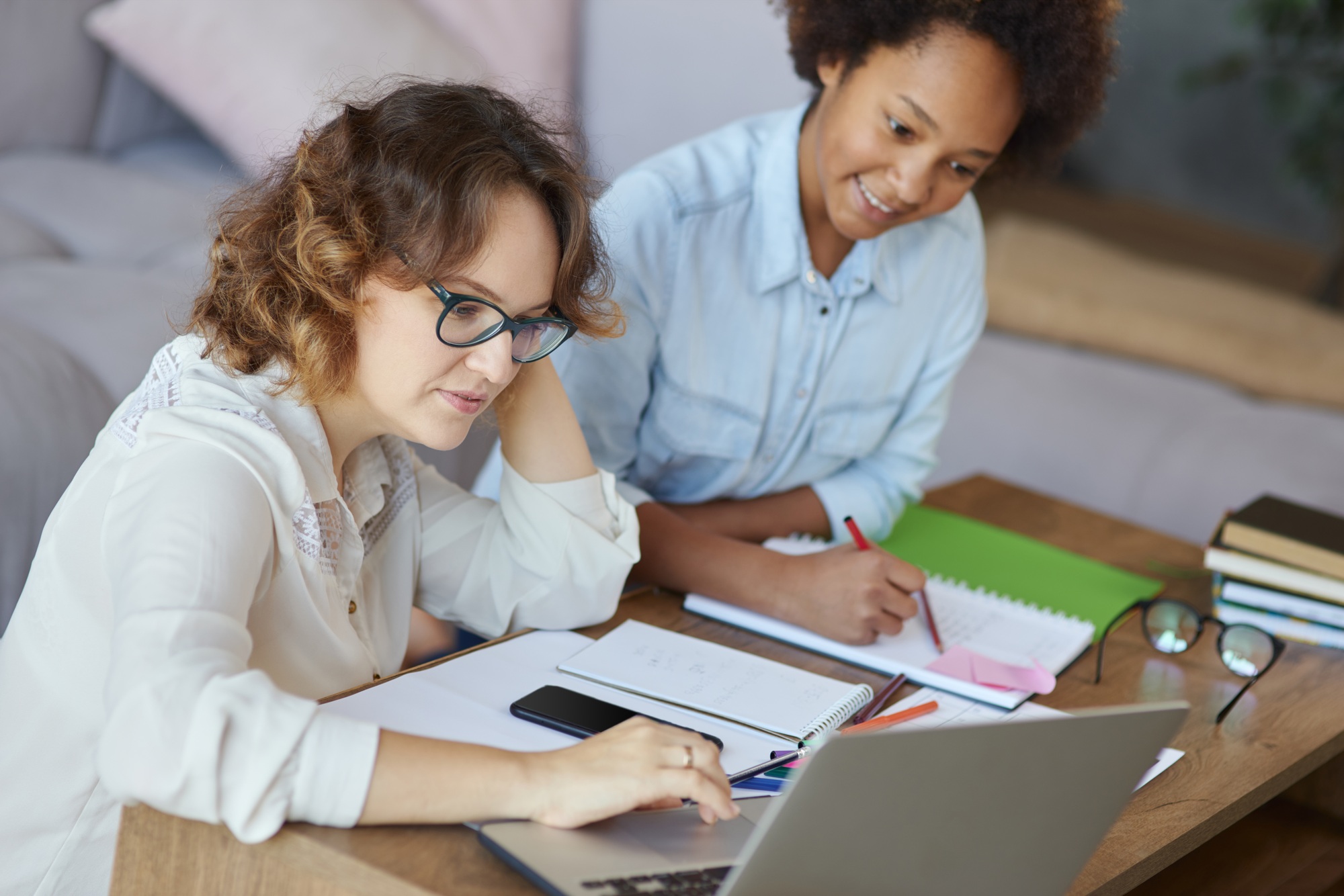 Portrait of focused female teacher in glasses helping teen schoolgirl with homework, sitting at the